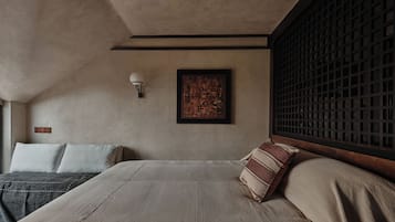 A bedroom with a bed, pillows, a wall-mounted light, and a framed artwork.