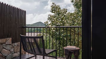 A wooden deck with a chair and a small table, a stone wall, and a view of a hill and trees.