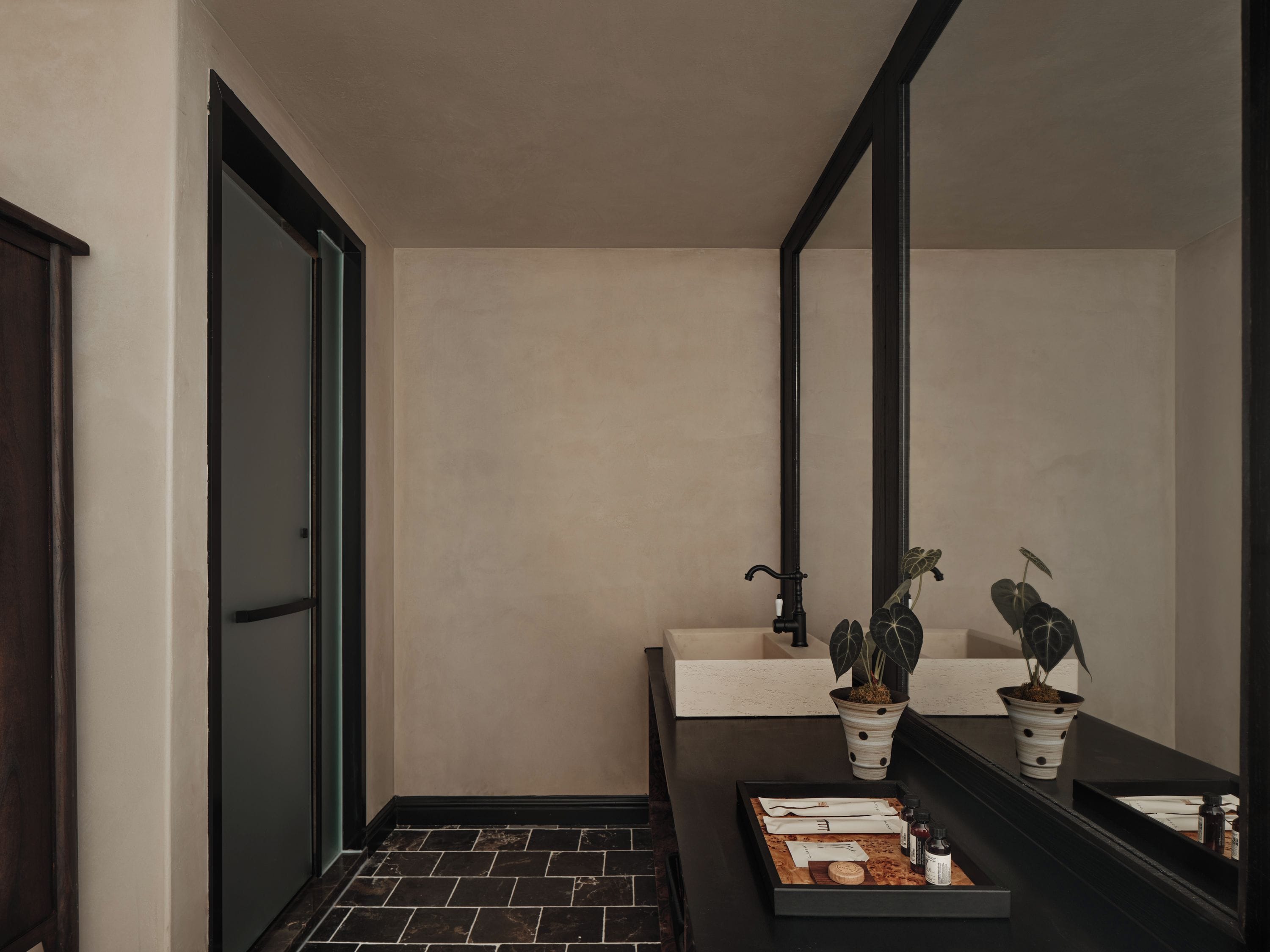 A bathroom with a dark floor, a mirror, a sink, and two potted plants.