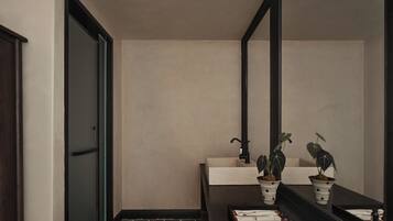 A bathroom with a dark floor, a mirror, a sink, and two potted plants.