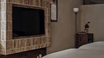 Habitación con una televisión instalada en una pared de azulejos, una mesita de noche con lámpara y una cama con cubierta blanca.