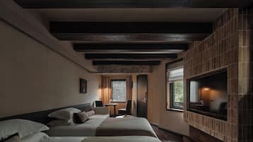 A hotel room with a large TV, two beds, a small table, and a fireplace.