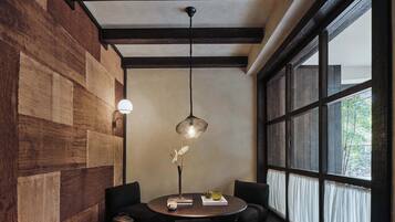 A room with a round table, two chairs, a hanging light fixture, and a large window with curtains.