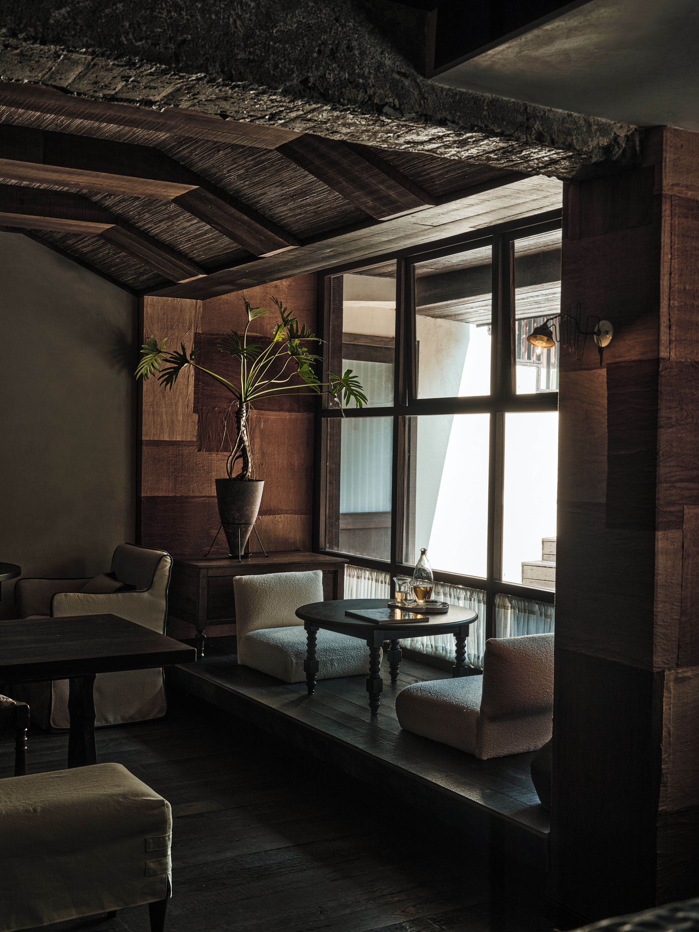 A cozy interior with a wooden ceiling, large windows, and a potted plant.