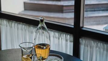 Una mesa con una botella, vasos y un plato con algo verde, frente a una ventana que da a una escalera.