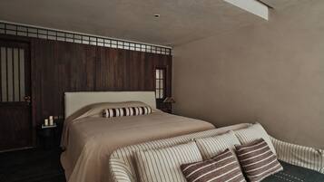 A bedroom with a large bed, a bedside table with a lamp, and a view of the outside through a window.