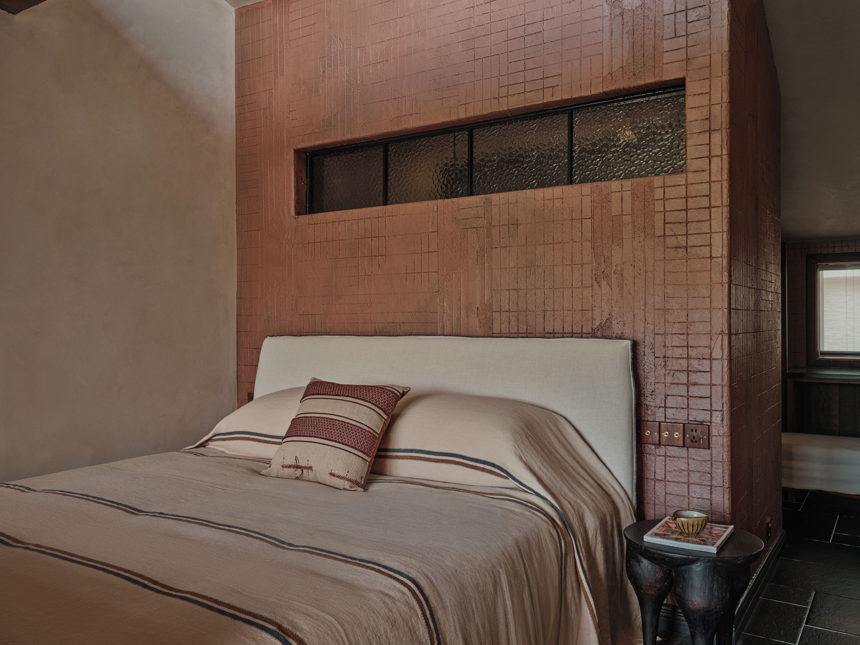 A bedroom with a bed, a nightstand, a window, and a brick wall.