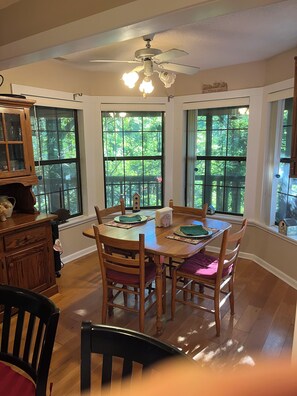A dining area with a wooden table and chairs, large windows with a view of greenery, and a ceiling fan. - Mountain Refuge “Lord, You have been our refuge in every generation.”Ps 90:1 (Franklin)