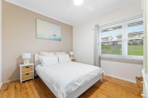 Ein Schlafzimmer mit einem Bett, Nachttischen, einem Gemälde und einem Fenster mit Jalousien.
