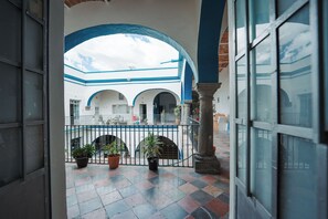 Un patio interior con suelo de baldosas, plantas en macetas y una valla de metal.