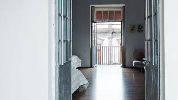 A hallway with a bed, a door, and a view of an outdoor area.