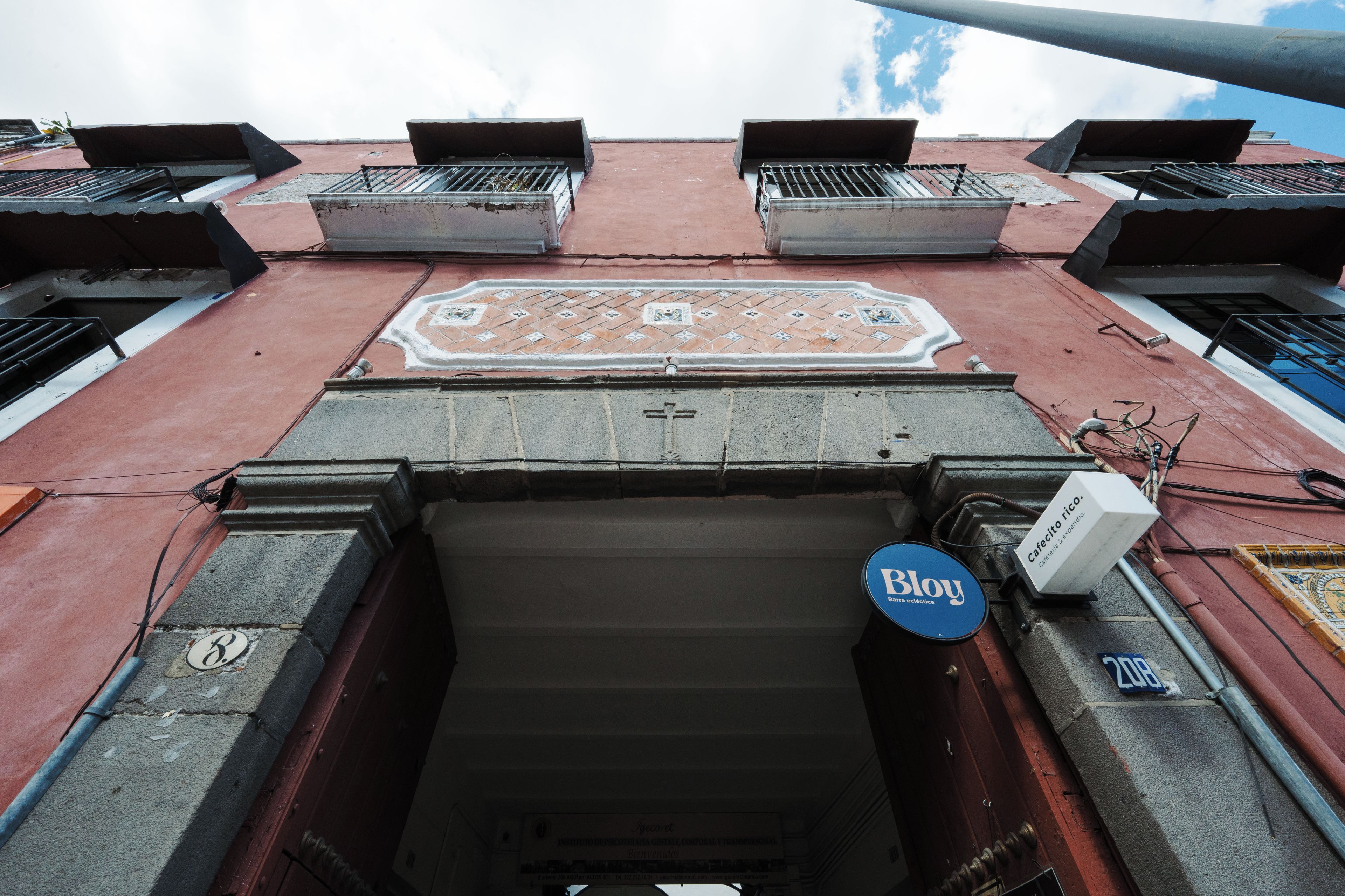 A building entrance with a tiled decorative pattern, a door with a metal handle, and a sign that reads 'Bloy'.