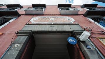 A building entrance with a tiled decorative pattern, a door with a metal handle, and a sign that reads 'Bloy'.