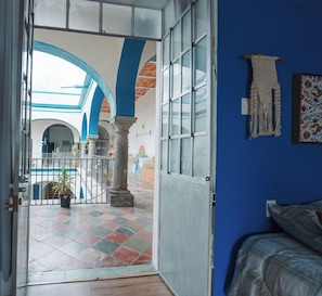 An interior view of a room with a large open doorway leading to an outdoor area with a tiled floor and blue arches. - Vrbo Property (Heroica Puebla de Zaragoza)