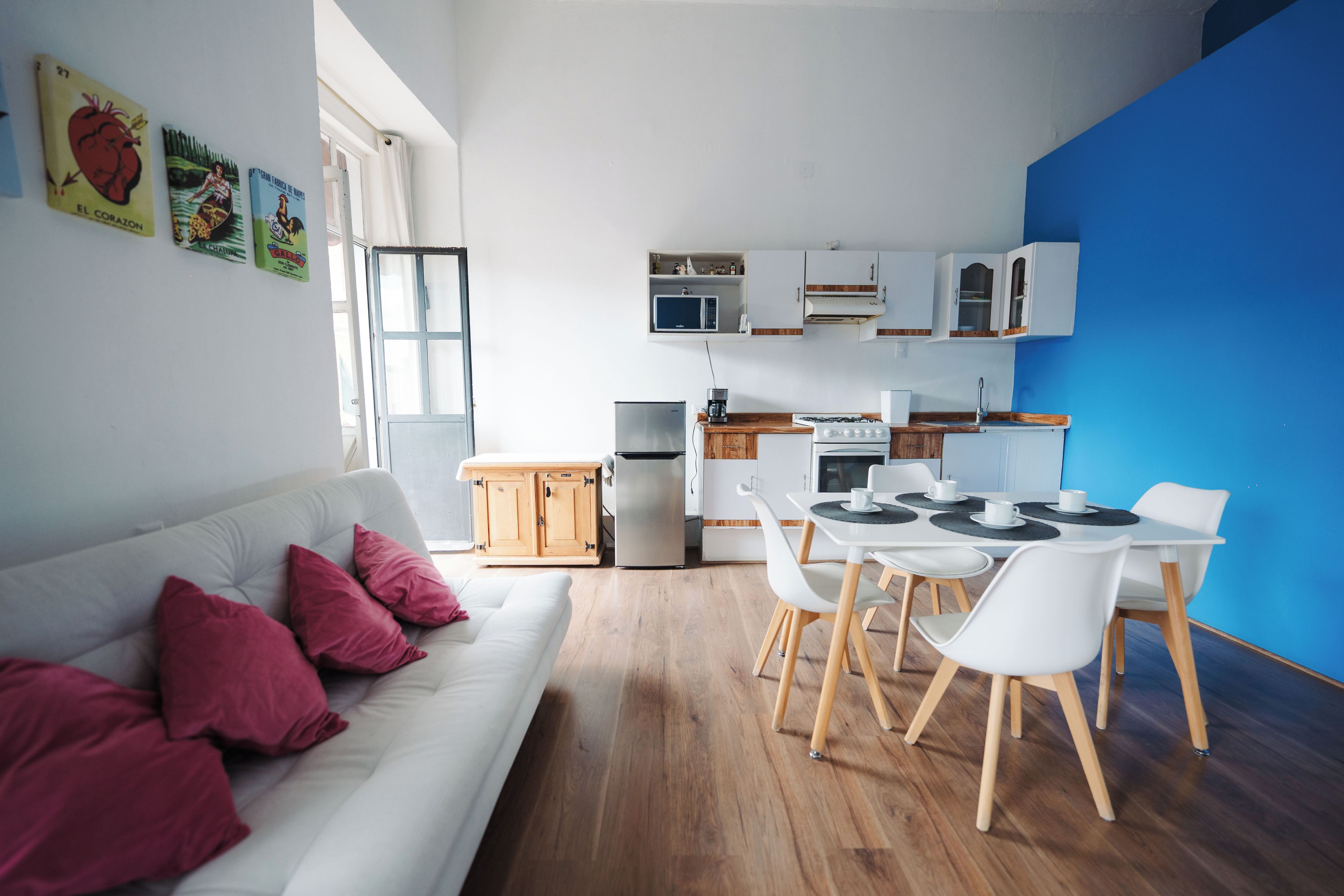 A compact living space with a kitchenette, dining area, and a sofa with red cushions.
