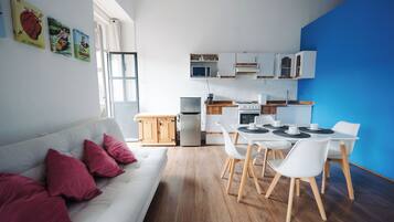 A compact living space with a kitchenette, dining area, and a sofa with red cushions.