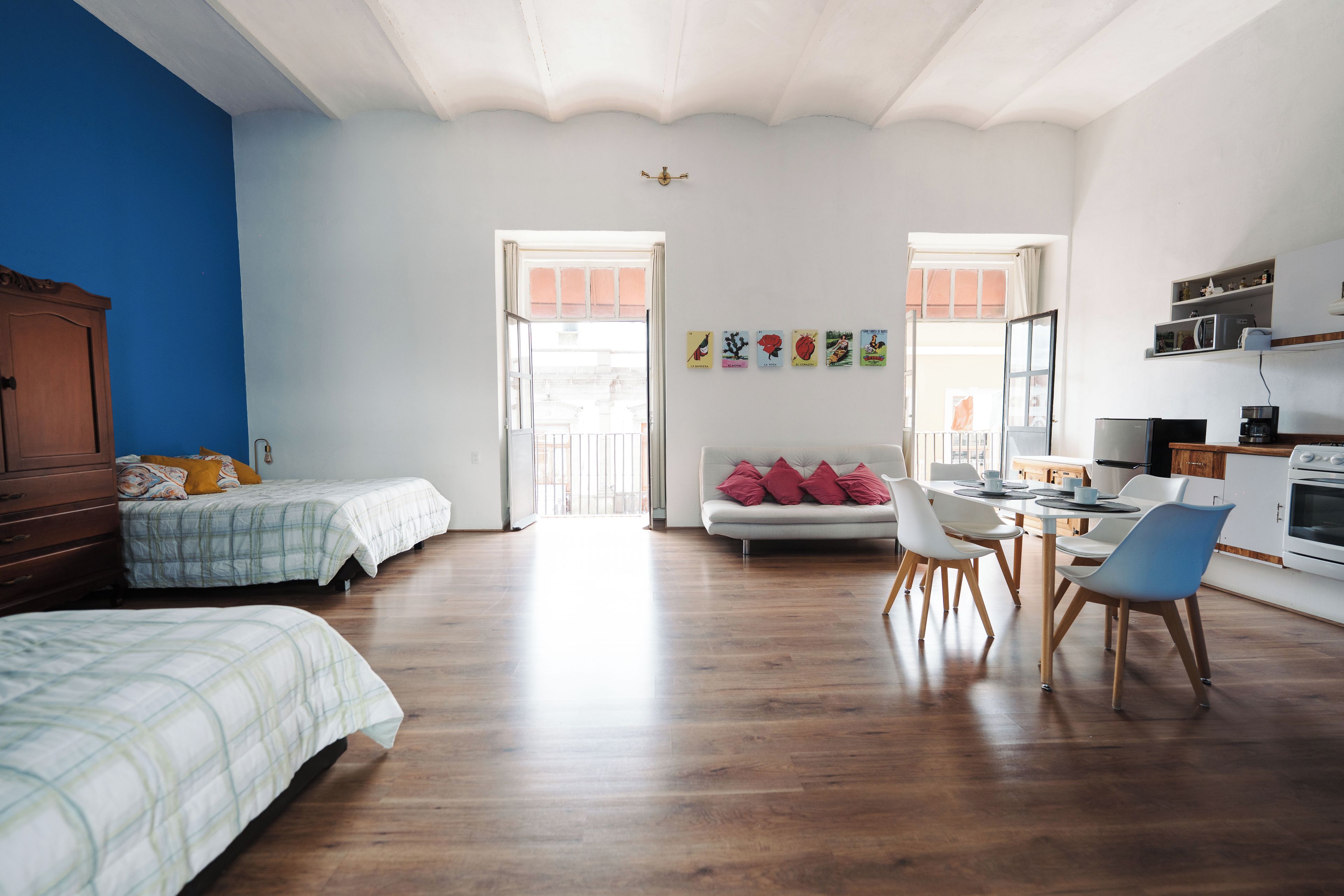 A spacious room with a wooden floor, a bed, a sofa, a dining table with chairs, and a kitchenette.