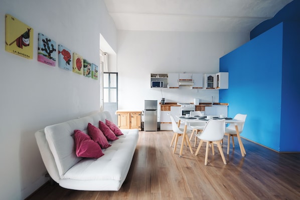 A modern living space with a white sofa, a dining area with white chairs, a kitchen with white cabinets, and a blue accent wall. - Vrbo Property (Heroica Puebla de Zaragoza)