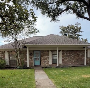 A brick house with a front porch, a door, and a small tree in the yard. - Beautiful 3BR Home Near Dallas Perfect for Families & Groups (Garland)