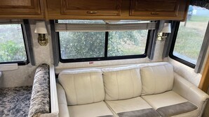 Een gezellig interieur van een camper met een bank, een getextureerd vloerkleed en houten kasten.