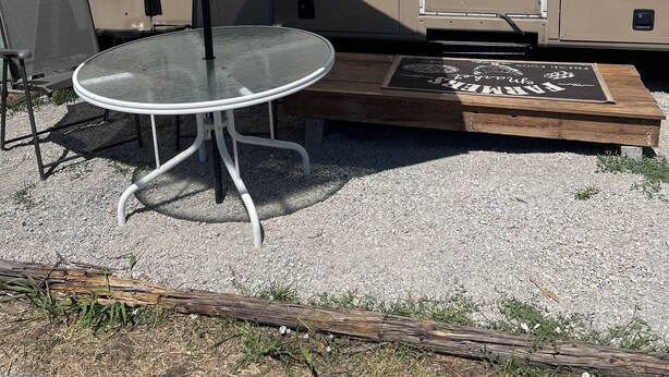 Een recreatiewagen met een tafel, een parasol, een bankje en een bord.