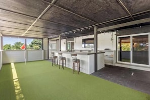Un área de bar al aire libre con suelo verde, taburetes de bar y una barra.
