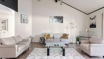 A modern living room with a sofa set, a glass coffee table, and a white shag rug.
