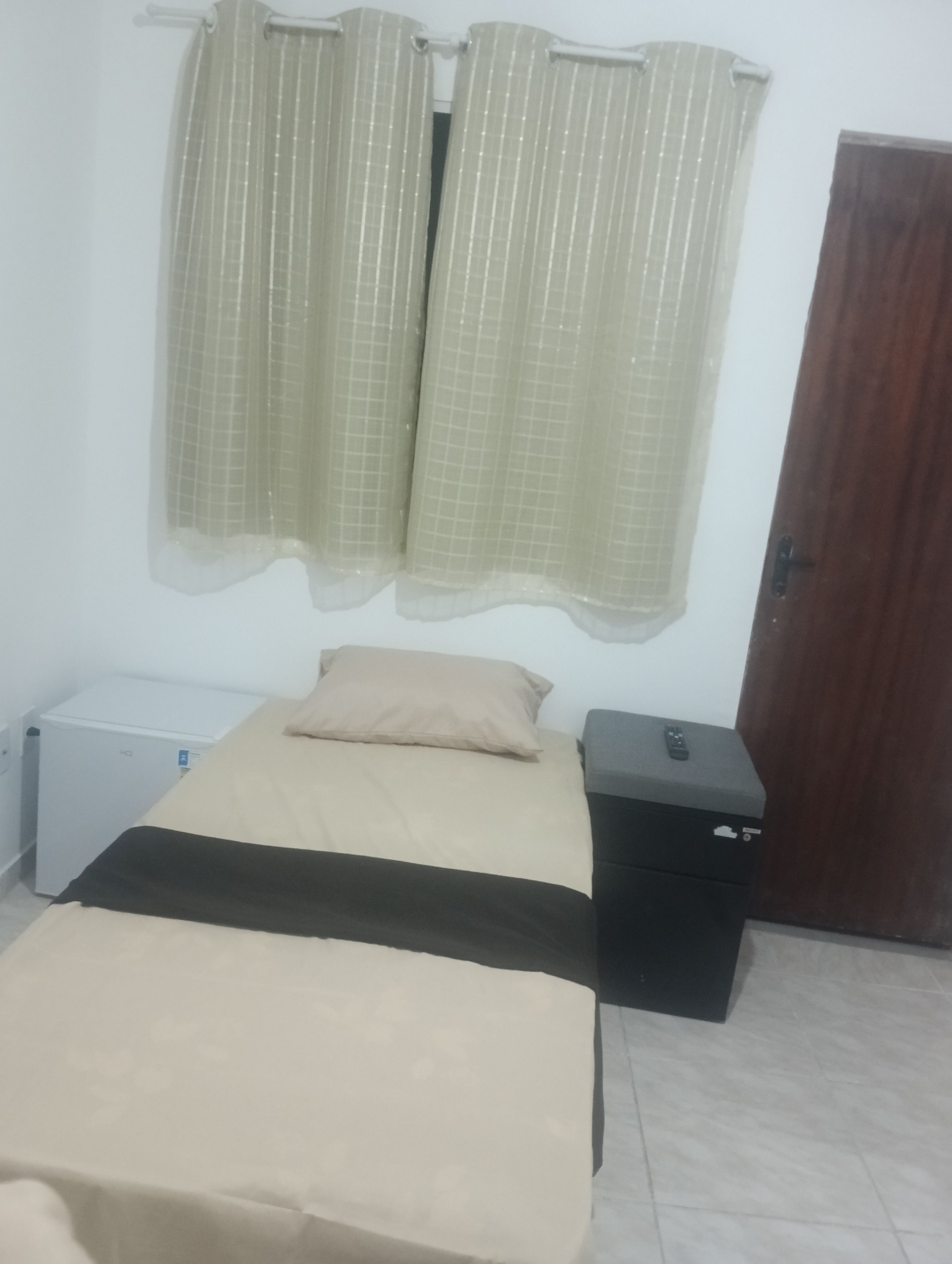 A bedroom with a bed, a small bedside table, a heater, and a door.