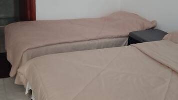 A room with two beds, each with a beige bedspread and pillows, a small bedside table, and a door with a red frame.