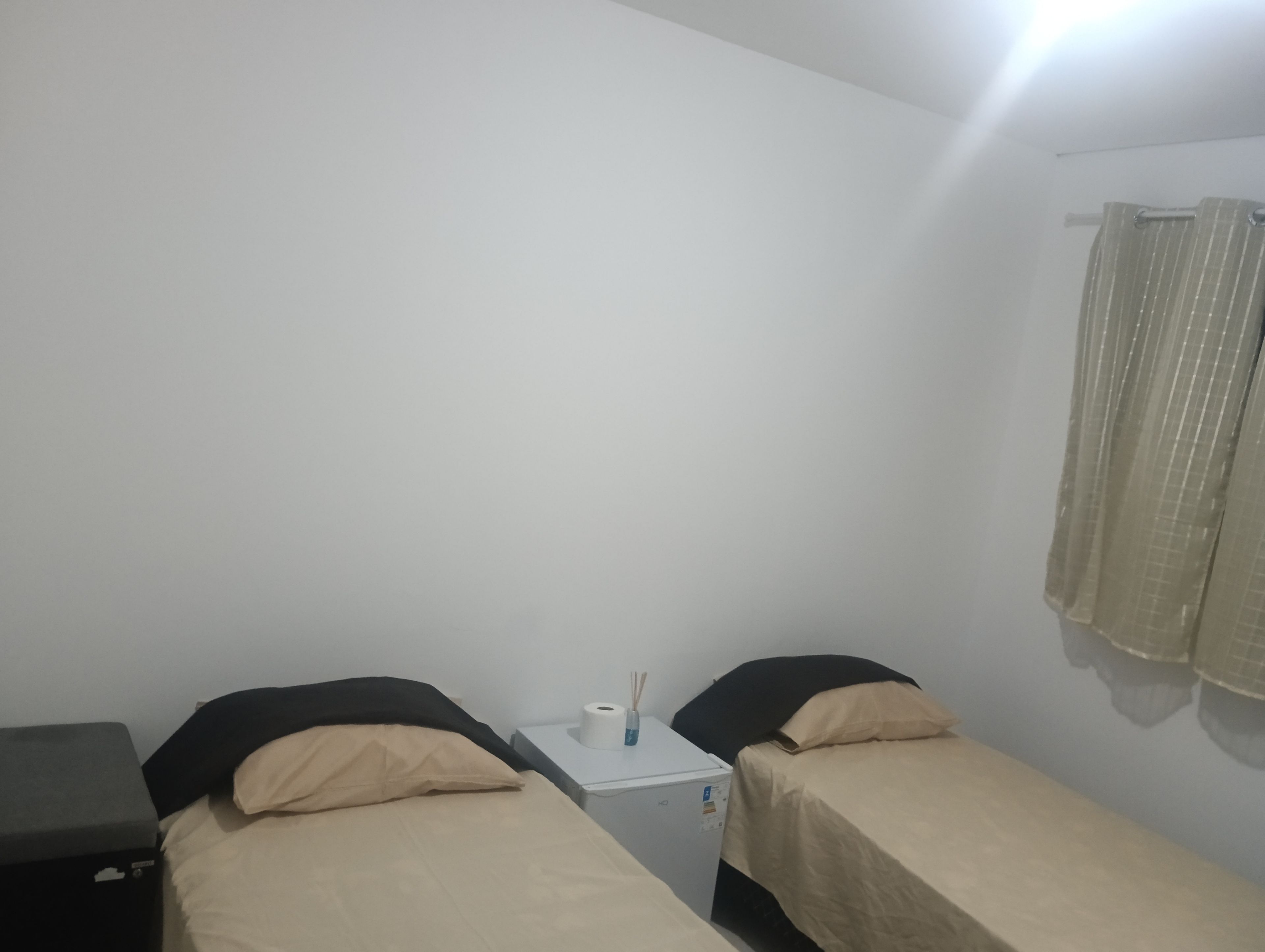 A small, single-room accommodation with two beds, a nightstand, and a curtain.