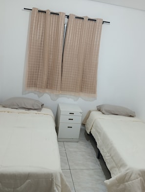 A bedroom with two beds, a nightstand, and a window with curtains.