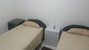 Quarto com duas camas de solteiro, um aquecedor pequeno branco e uma mesinha de cabeceira escura.
