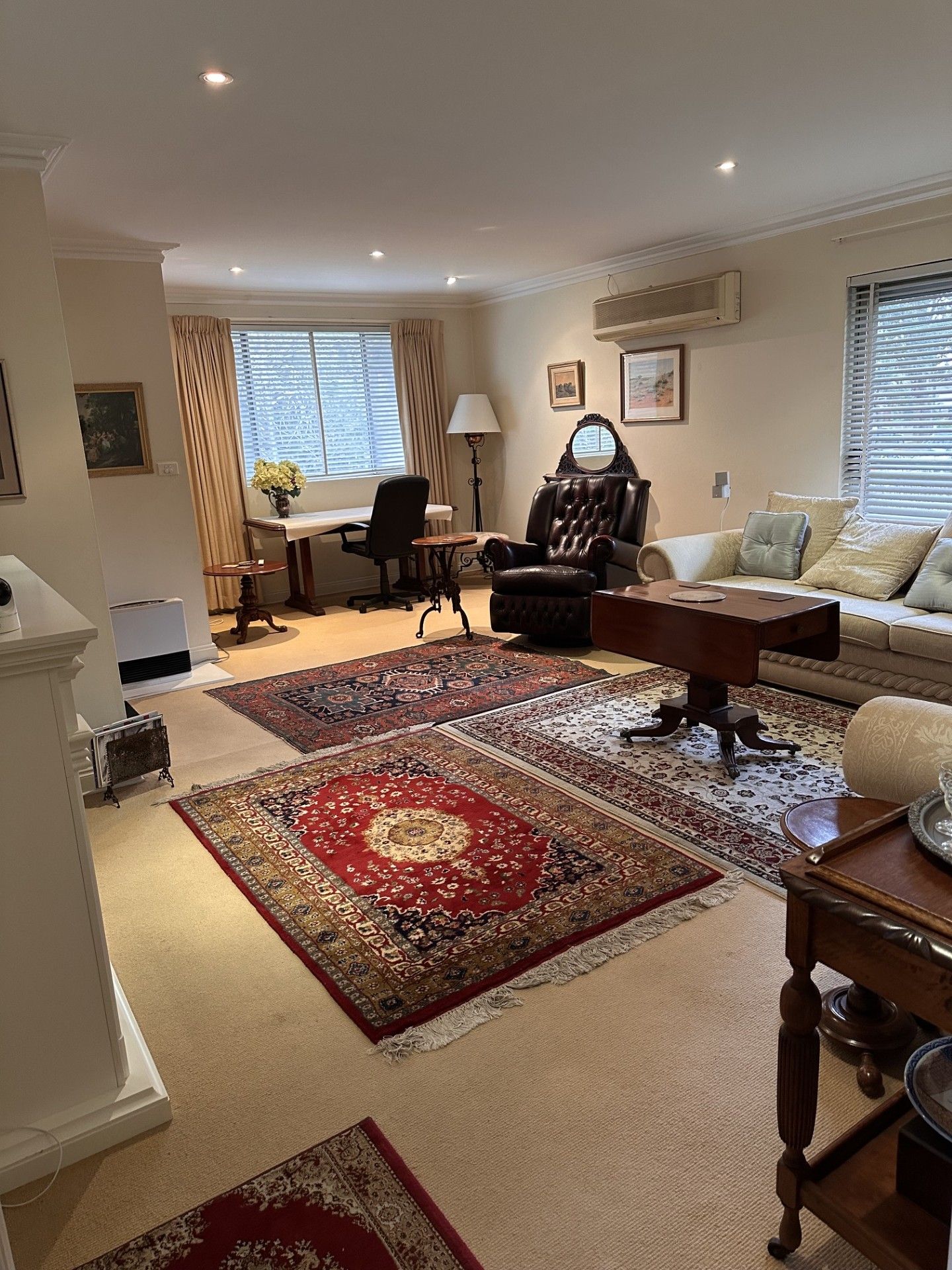 A living room with a sofa, a chair, a coffee table, and a rug. There is a window with blinds, a lamp, and a picture frame on the wall.