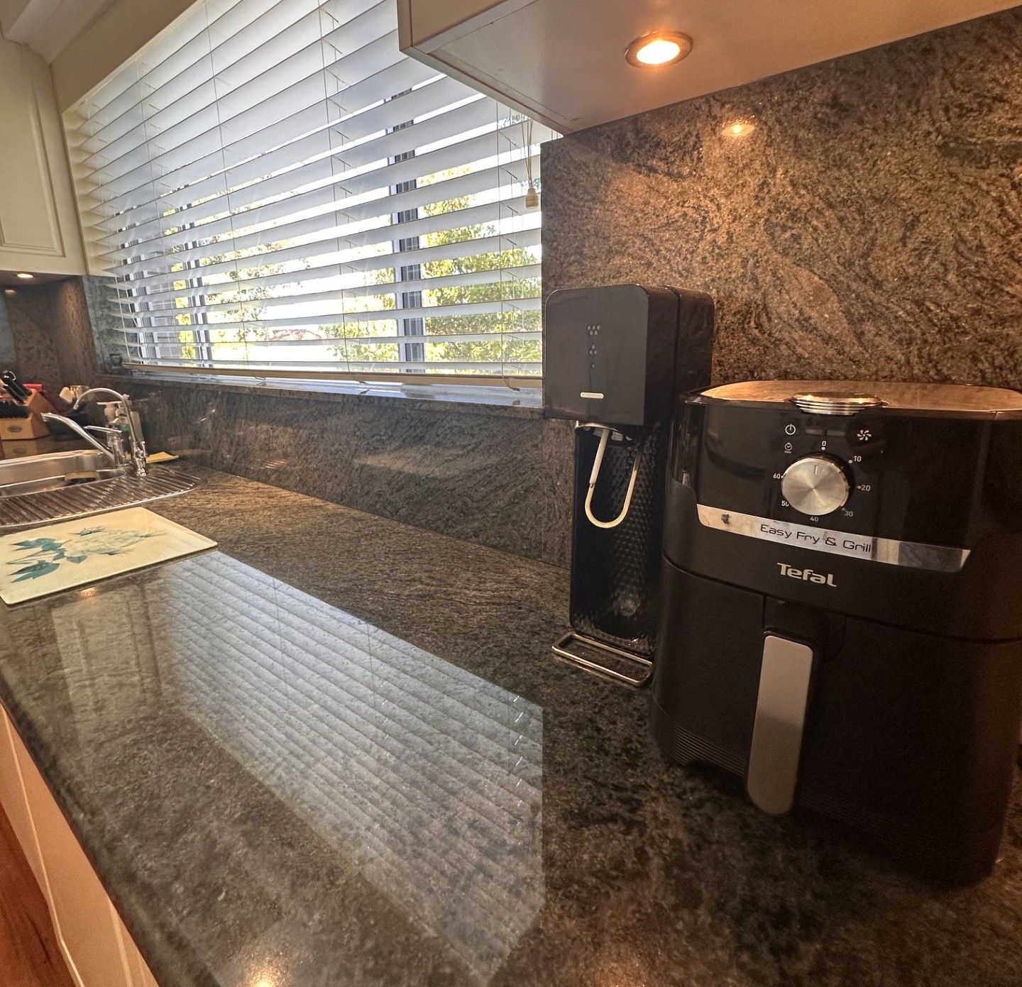 A kitchen with a granite countertop, a coffee maker, and a window with blinds.