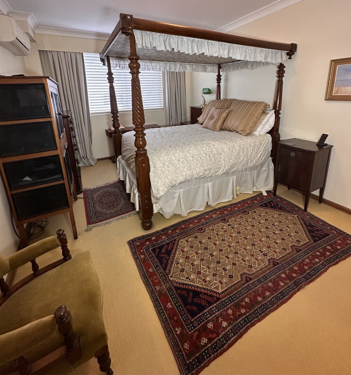 Un lit à baldaquin avec un couvre-lit et des oreillers blancs, une table de chevet en bois, un bureau avec une lampe, une chaise et un grand tapis à motifs.