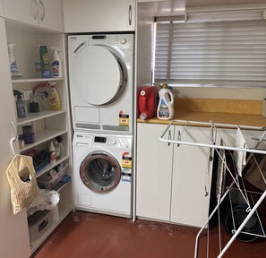 Un espace buanderie compact comprenant un lave-linge à chargement frontal, un étendoir et des étagères remplies de produits de nettoyage.