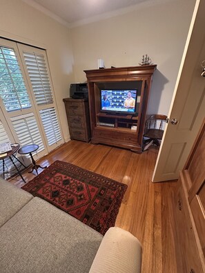 Un salon avec un téléviseur posé sur un meuble en bois, un tapis à motifs, un canapé et une porte.