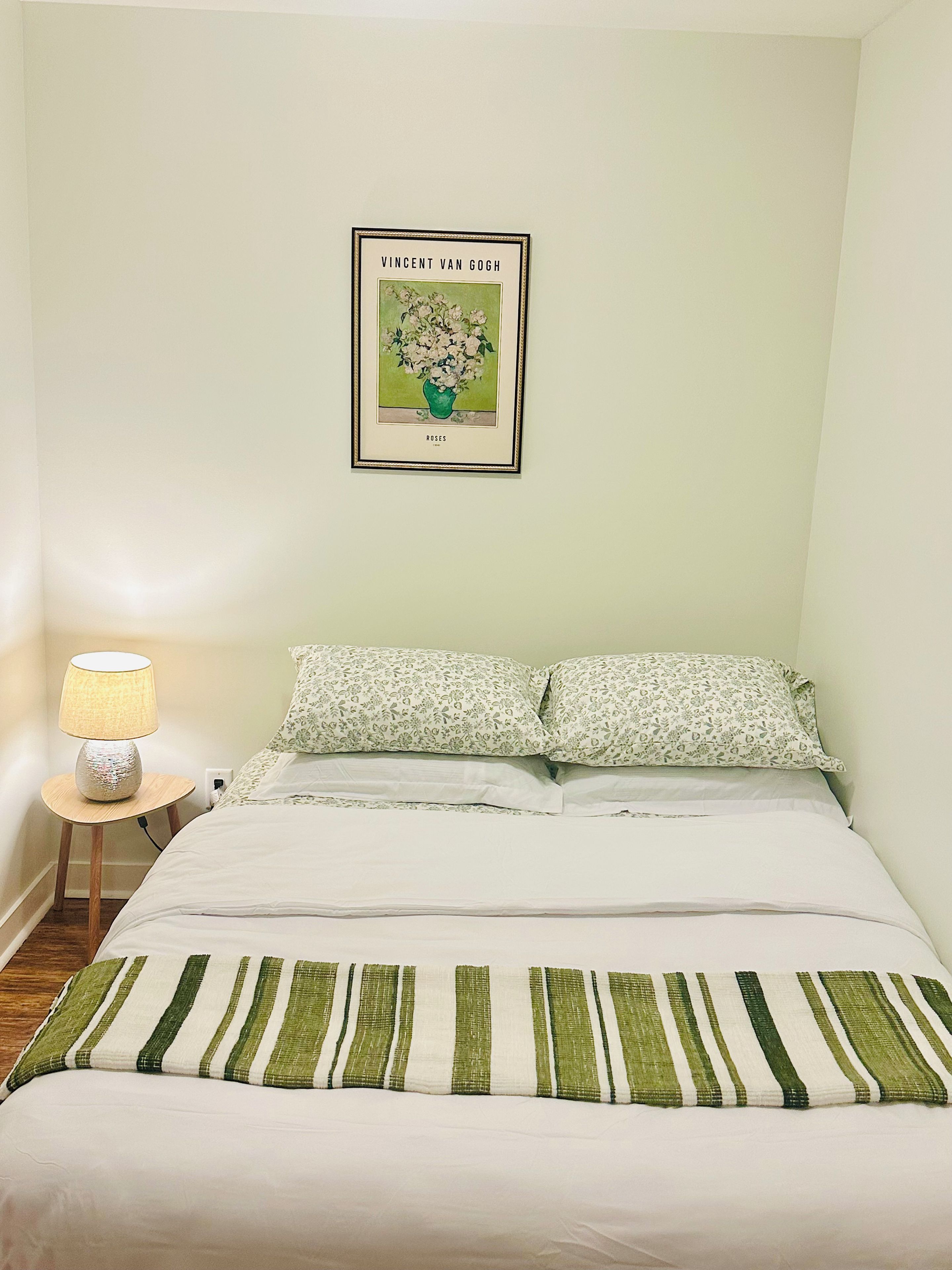 Una camera da letto con un letto, cuscini, una lampada da comodino e un quadro appeso al muro.