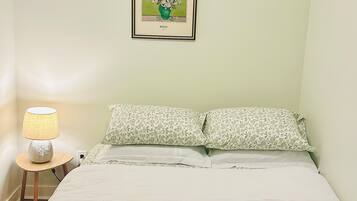 Una camera da letto con un letto, cuscini, una lampada da comodino e un quadro appeso al muro.