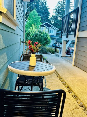 A patio with a round table and chairs, a vase with flowers, and a view of a residential street.