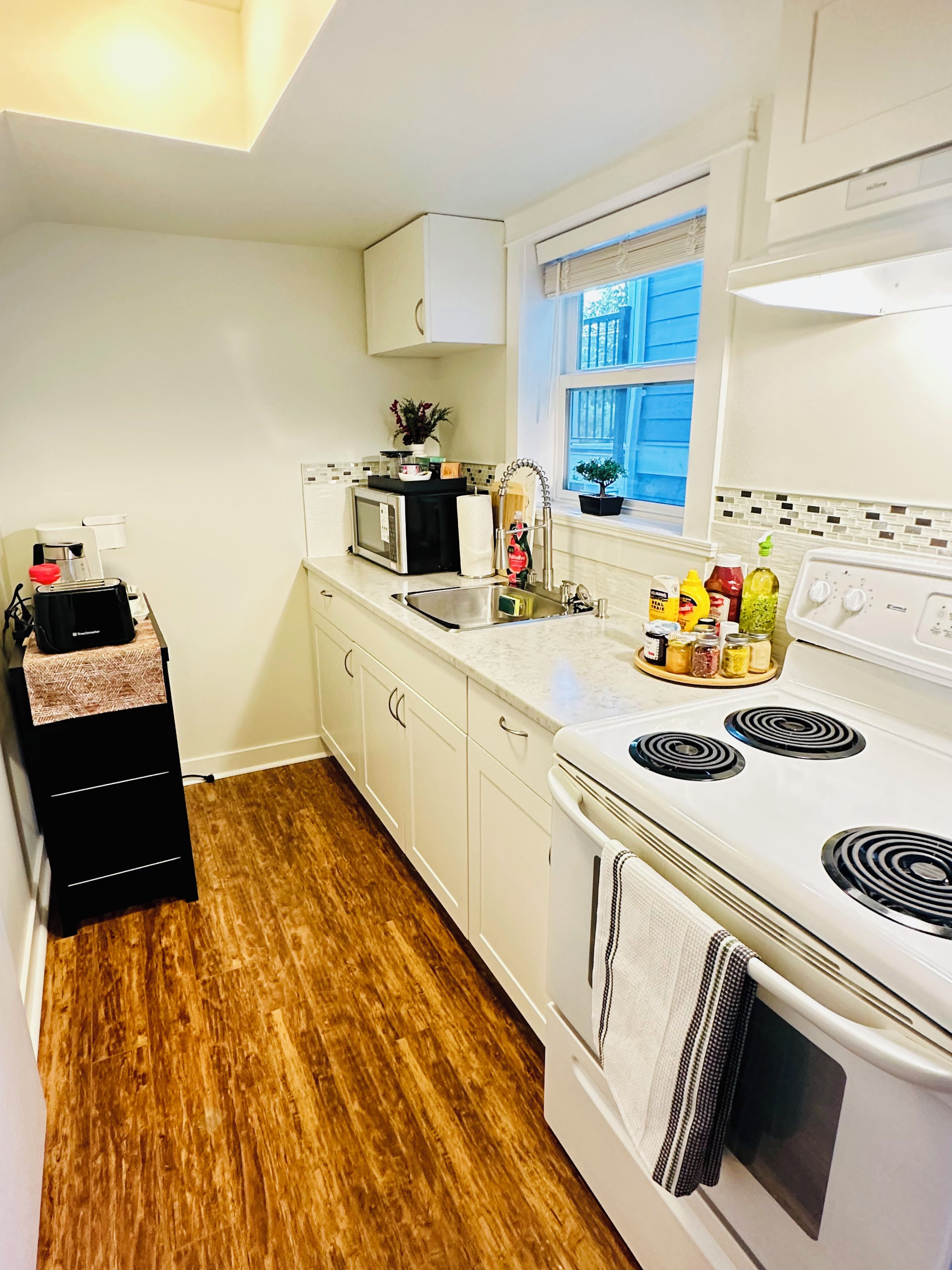 A compact kitchen with white cabinets, a microwave, a stove, and a sink.
