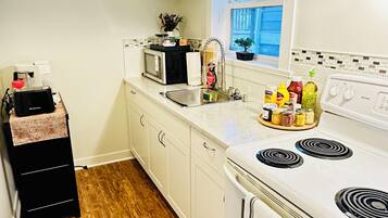 A compact kitchen with white cabinets, a microwave, a stove, and a sink.