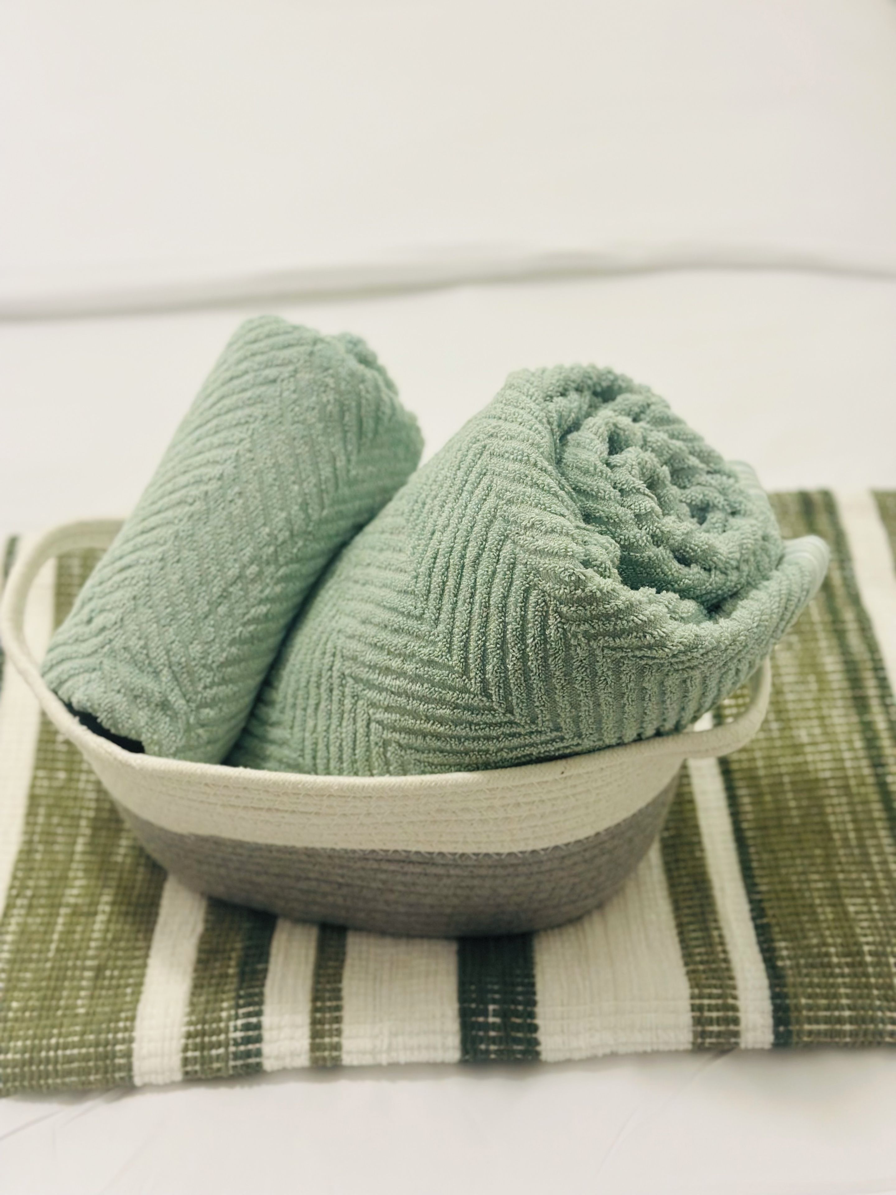 A bowl containing two rolled towels placed on a striped cloth.