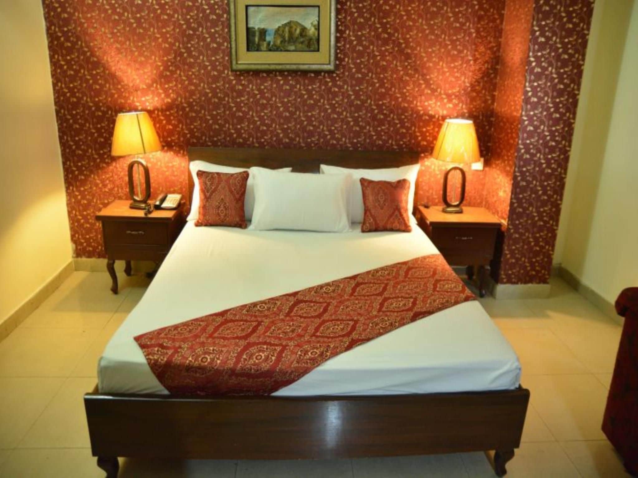 A hotel room with a large bed, two bedside tables, and a patterned wall.