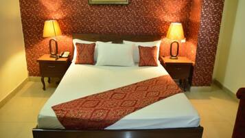 A hotel room with a large bed, two bedside tables, and a patterned wall.