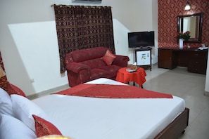 A hotel room with a bed, a sofa, a TV, a small table, and a mirror. - Luxury One Hotel Lahore (Lahore)