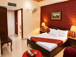 A hotel room with a large bed, two bedside tables with lamps, a red patterned wall, a framed picture, and a wooden bench. - Luxury One Hotel Lahore (Lahore)