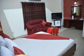 Una habitación de hotel con cama, sofá, televisor, una mesita y un espejo.