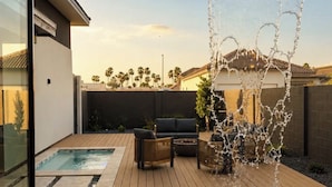 Ein Garten mit Schwimmbad, Holzterrasse, Gartenmöbeln und einem Wasserspiel.