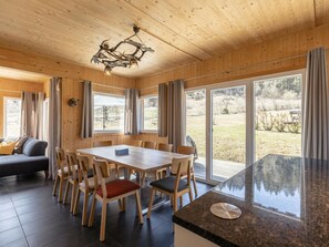 Ein Holzinterieur mit einem Esstisch, Stühlen, einer Couch und einem großen Fenster mit Blick ins Freie.